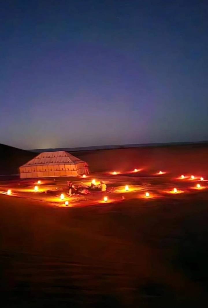Low-resolution night image of a candle-lit seating area beside a tent in the desert.