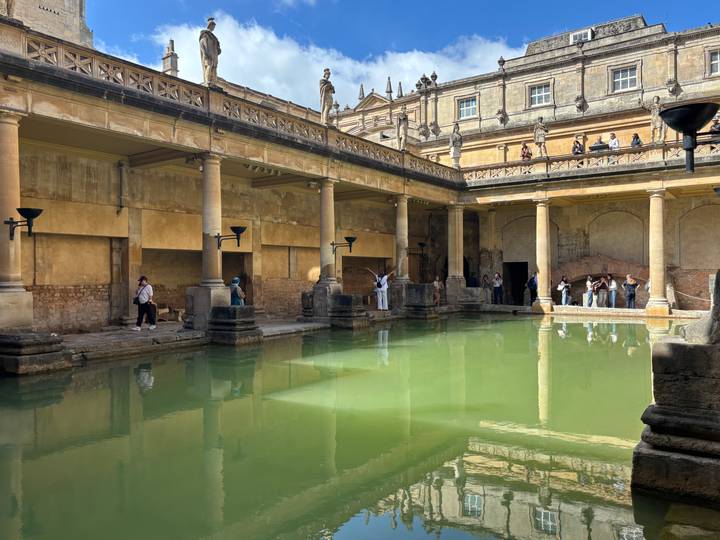 Interior of the Roman Baths with green thermal water and visitors exploring the colonnaded pool.