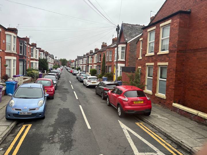 Long terraced residential street lined with parked cars and red-brick houses on an overcast day.