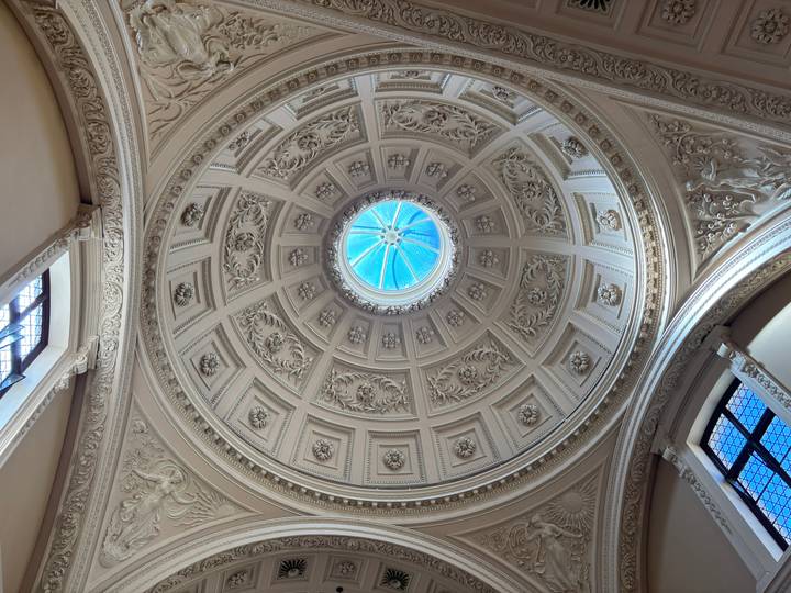 Ornate domed ceiling with intricate plasterwork and central skylight viewed from directly beneath.