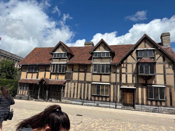 Timber-framed Shakespeare’s Birthplace house under a bright sky with a visitor in the foreground.