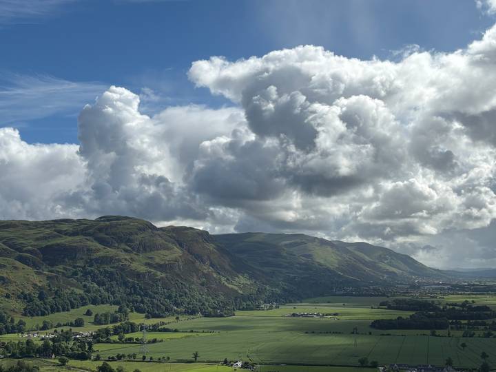 Dramatic green mountain ridge and valley under towering cumulus clouds.
