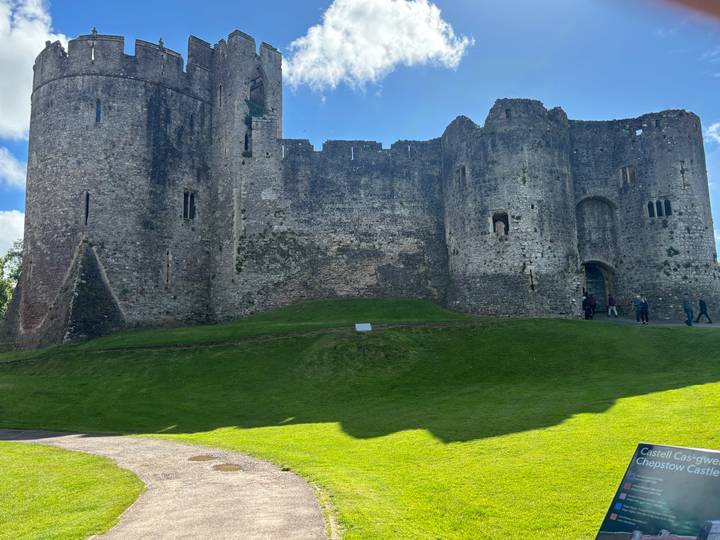 Massive stone castle ruin on a grassy slope with visitors walking near its base.
