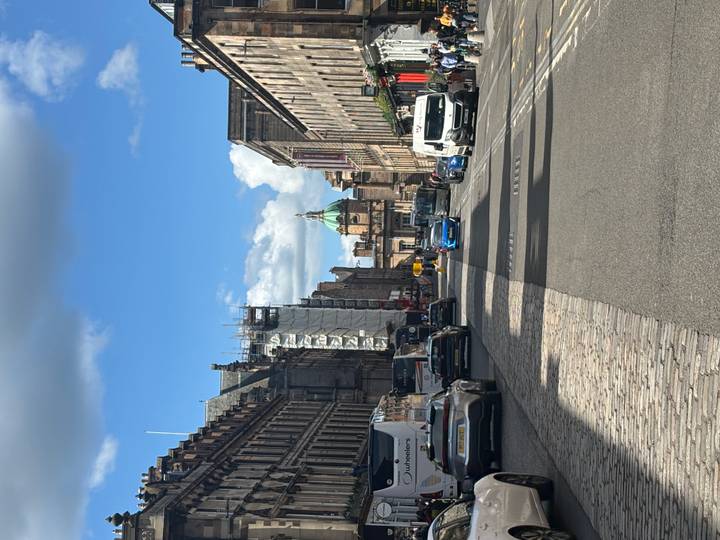 Wide Edinburgh street with historic stone buildings, vehicles and a distant domed courthouse.