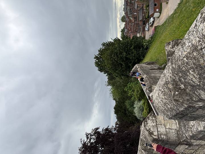 Visitors walking atop a medieval stone city wall overlooking rooftops under a grey sky.