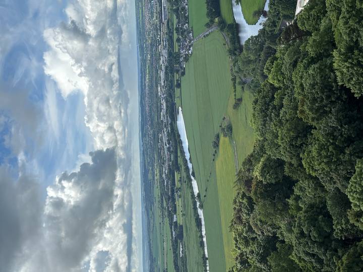 Elevated view of green fields, winding river and distant coast under layered clouds.
