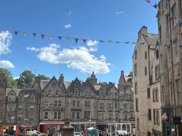 Row of sandstone tenements with festive bunting strung across a clear blue sky.