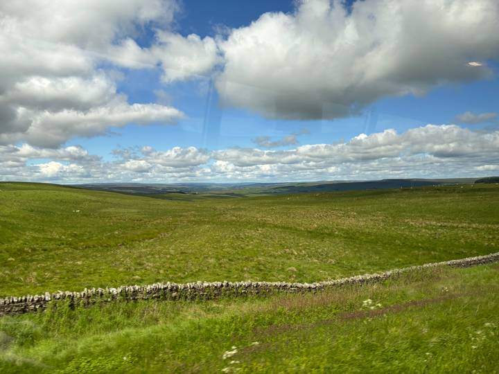 Wide grass-covered uplands and stone field walls stretching into a hazy horizon under fair-weather clouds.
