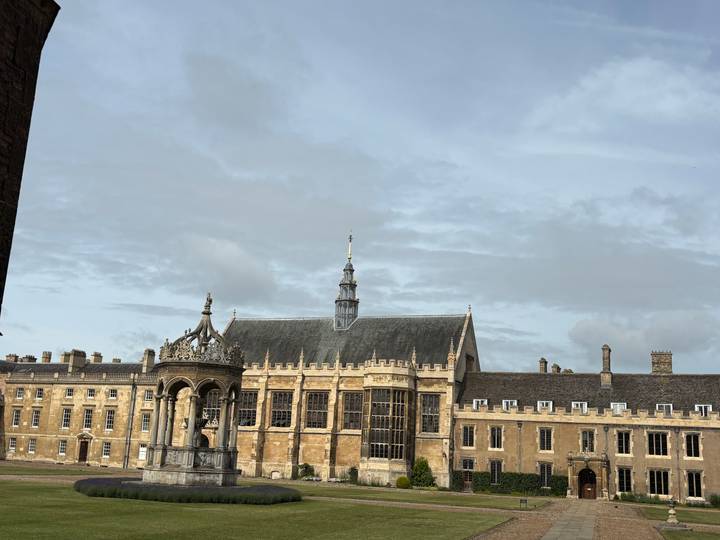 Historic collegiate courtyard with ornate fountain and stone buildings under a pale morning sky.