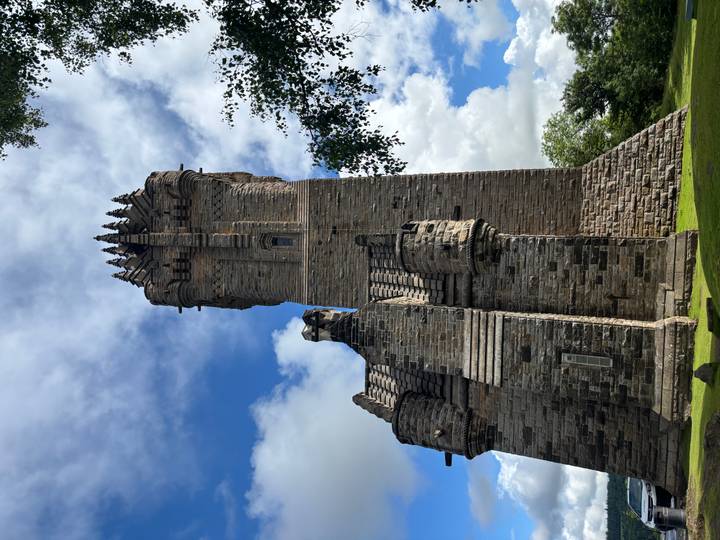 Tall stone tower of the Wallace Monument framed by blue sky and green lawn.