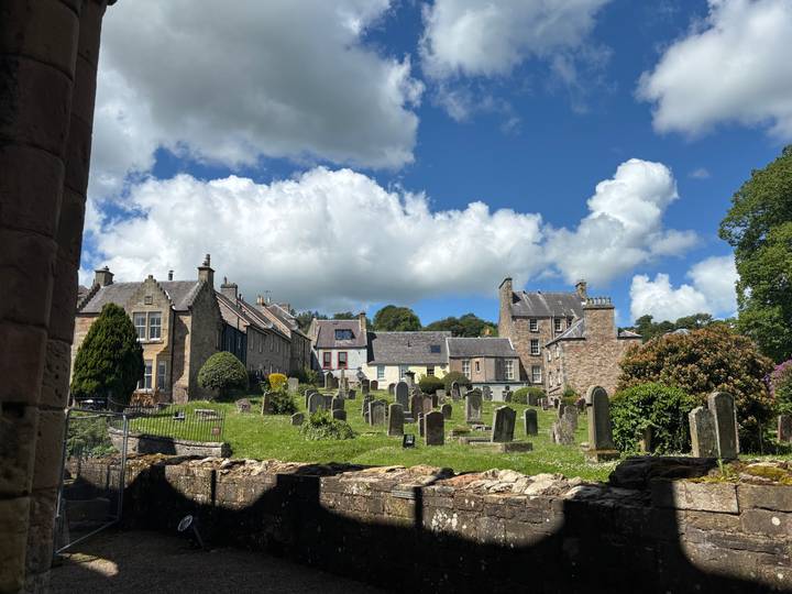 Quaint village churchyard with old gravestones, stone cottages and fluffy white clouds overhead.