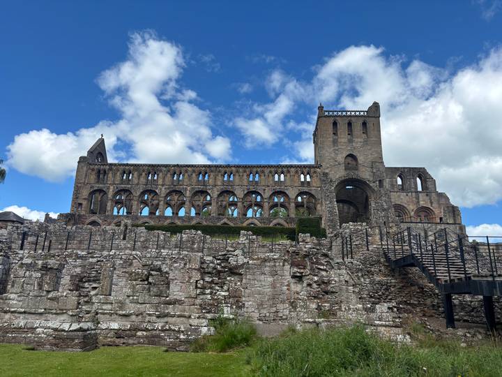 Extensive stone ruins of a Romanesque abbey with multiple arches set against a bright sky.