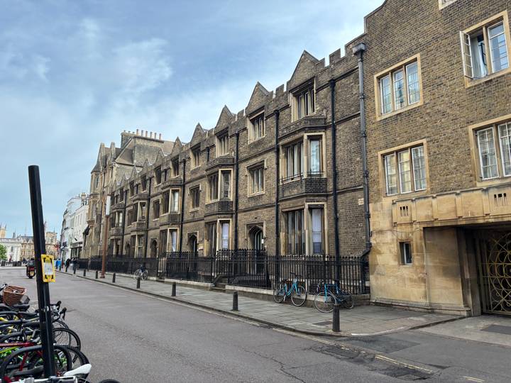 Row of historic stone college buildings with bicycles parked along a quiet Cambridge street.