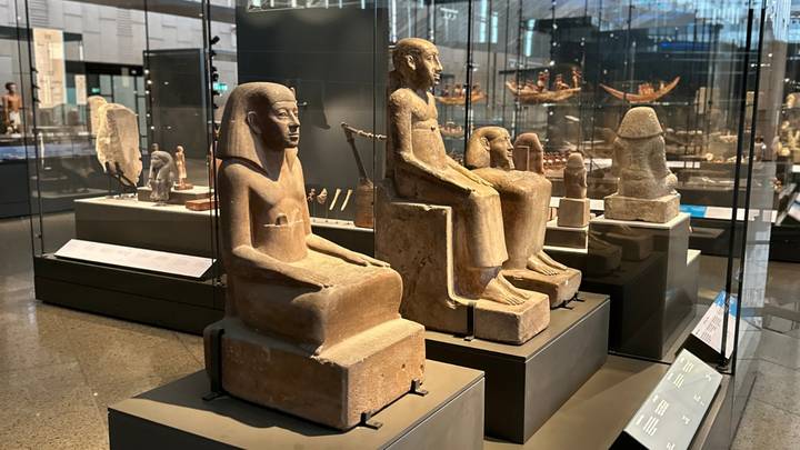Ancient Egyptian seated statues displayed in glass cases inside a modern museum gallery.