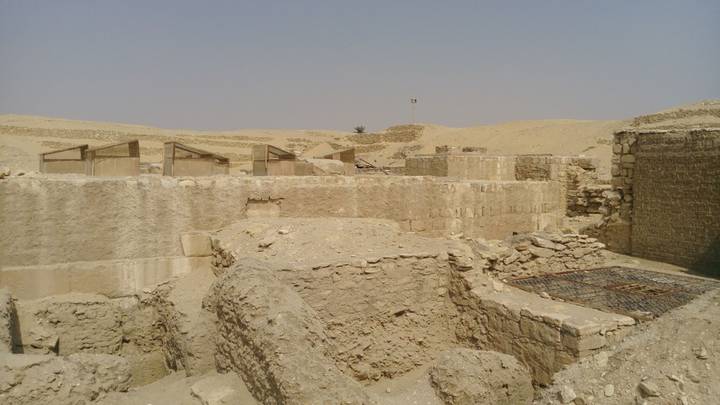 Sandy archaeological excavation of ancient settlement ruins amid barren desert landscape under hazy sky.