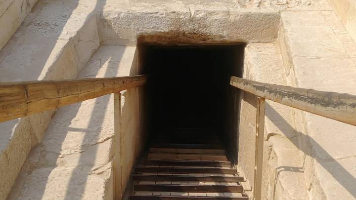 Wooden staircase descending into a dark stone shaft inside an ancient monument