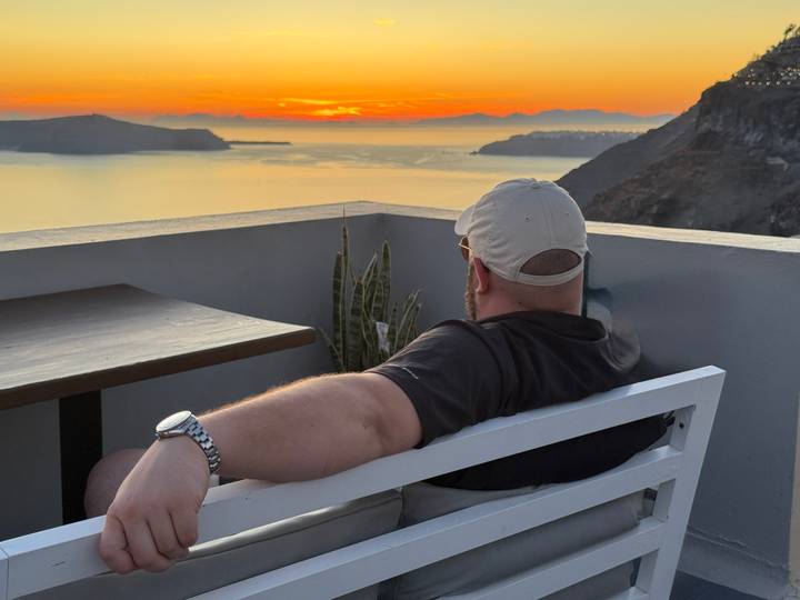 Man relaxing on a terrace bench watching the colorful Santorini sunset over the caldera