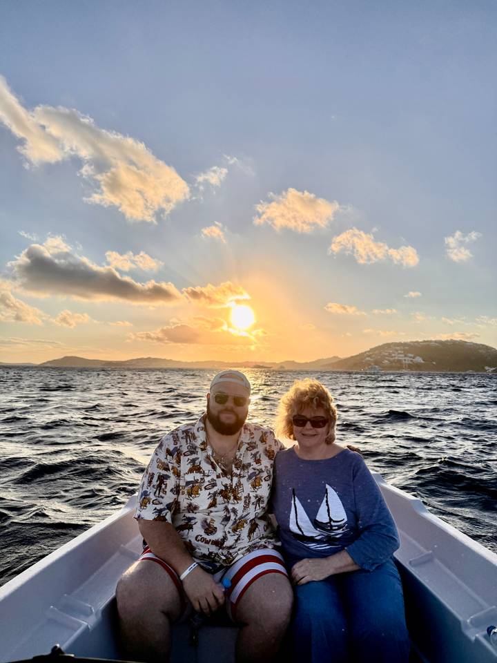 Couple posing on a boat with golden sunset over rolling hills and open sea