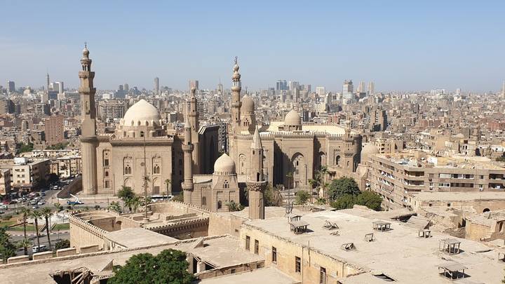 Panoramic view over Cairo featuring historic mosques with domes and minarets set against a sprawling modern skyline.