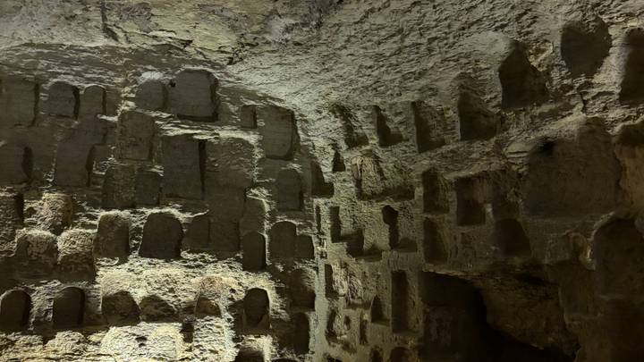 Dimly lit interior of an ancient rock-cut chamber with rows of carved niches in the walls.