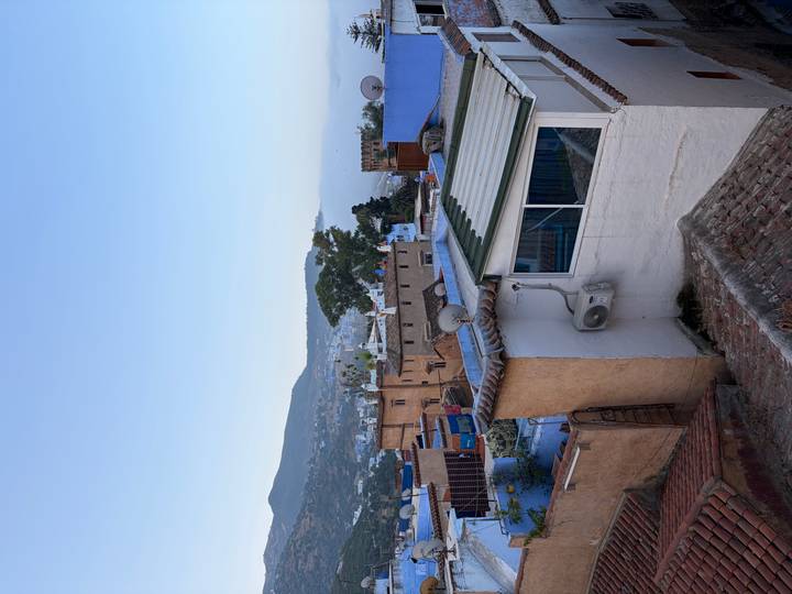Rooftop view over blue and earth-toned houses of Chefchaouen with mountains and mist in the distance.