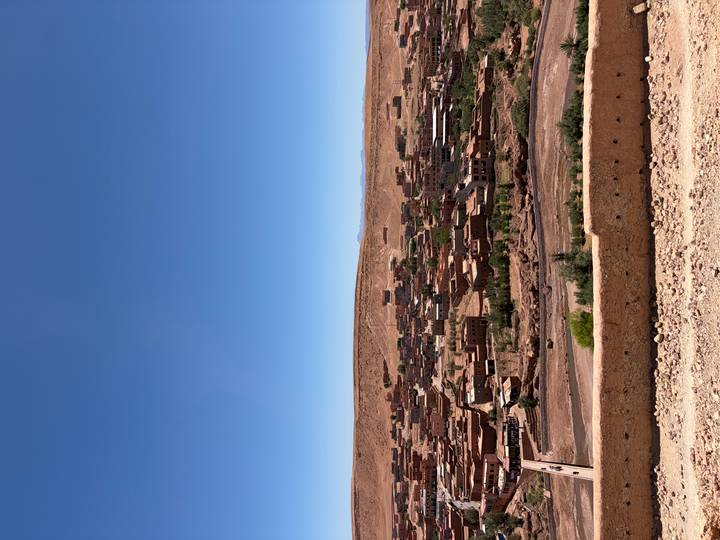 Panoramic view of an adobe desert town sprawled across arid hills under a clear blue sky.