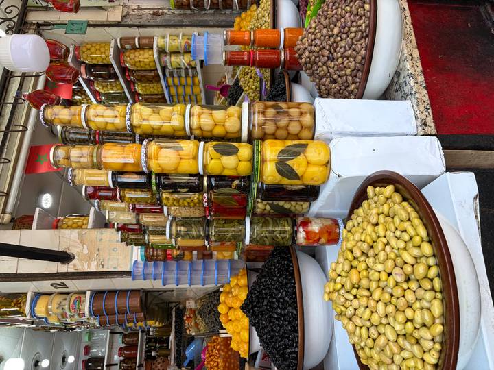 Vibrant display of olives and preserved vegetables stacked in jars at a Moroccan souk.
