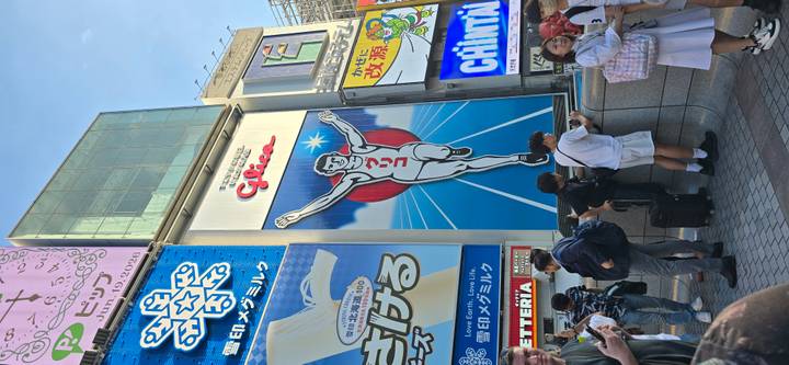 Iconic Glico running man billboard in Dotonbori Osaka surrounded by colorful advertisements and tourists taking photos.