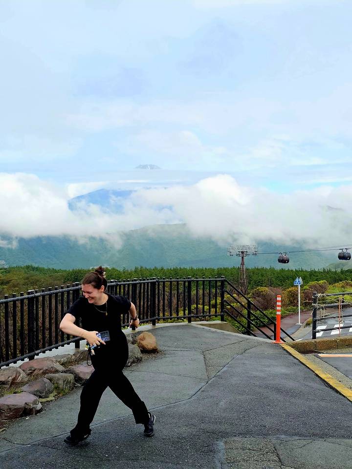 Smiling traveler near railing with mist-shrouded mountains, cable cars and Mount Fuji in the background