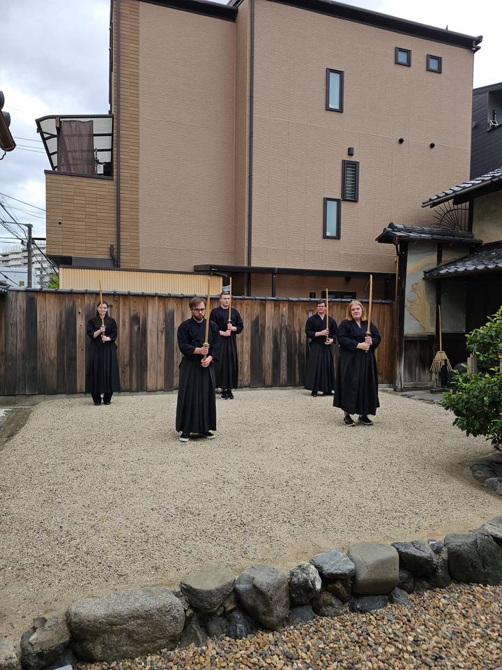 Group of participants in black martial-arts robes practicing sword stances in a courtyard