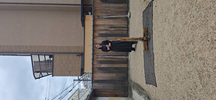 Single participant in robe standing beside wooden sword-cutting stand in gravel yard
