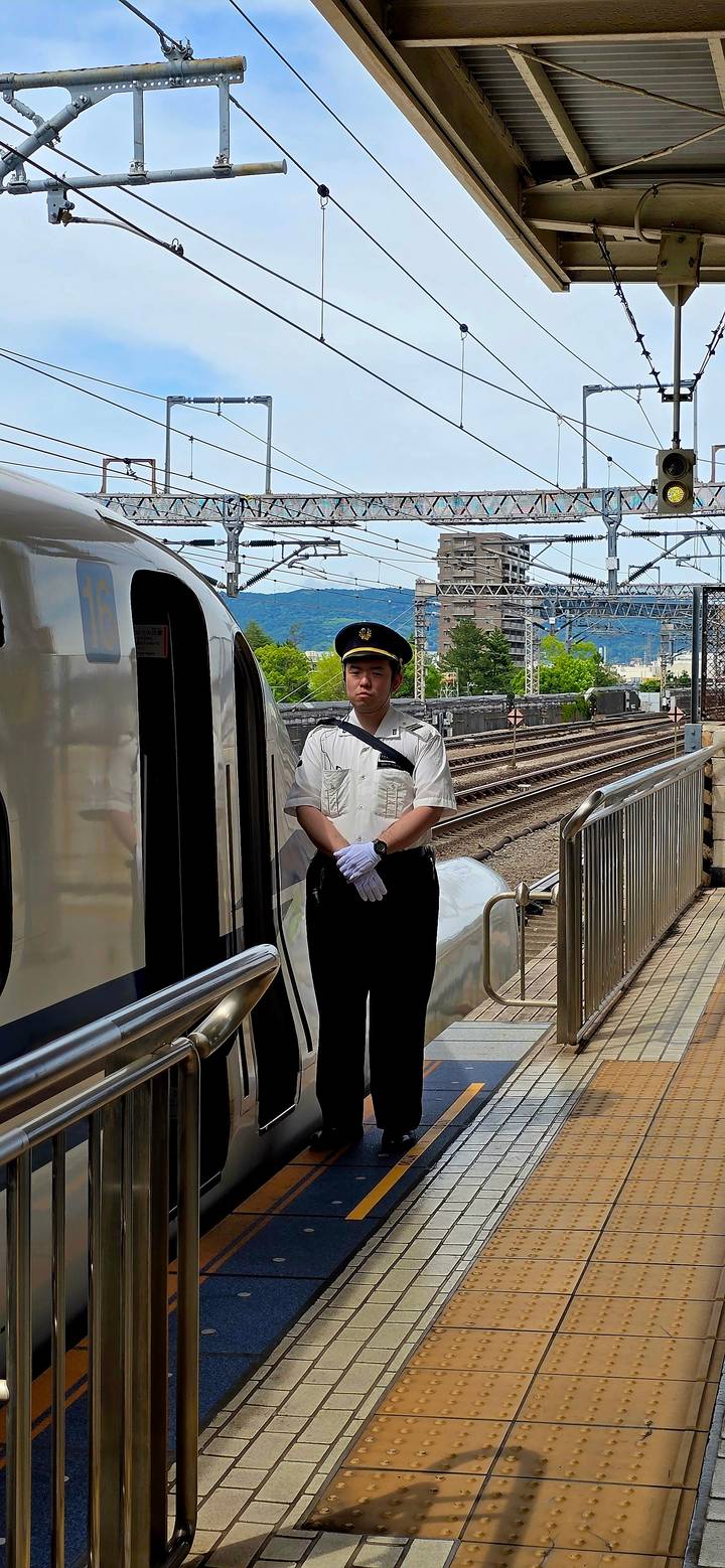 Uniformed train conductor standing beside sleek white carriage on station platform