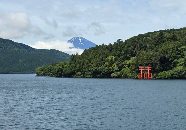 Serene lake with red torii gate on forested shore and snow-topped Mount Fuji rising behind