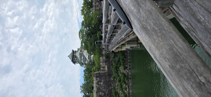 Osaka Castle rising behind a stone bridge over a green moat under mottled clouds