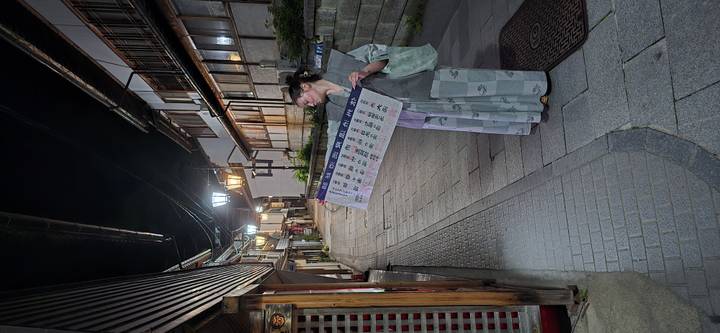 Traveler in yukata holding a long banner while exploring a quiet lantern-lit street at night
