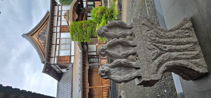 Stone sculpture of the three wise monkeys displayed on a pedestal outside a wooden building