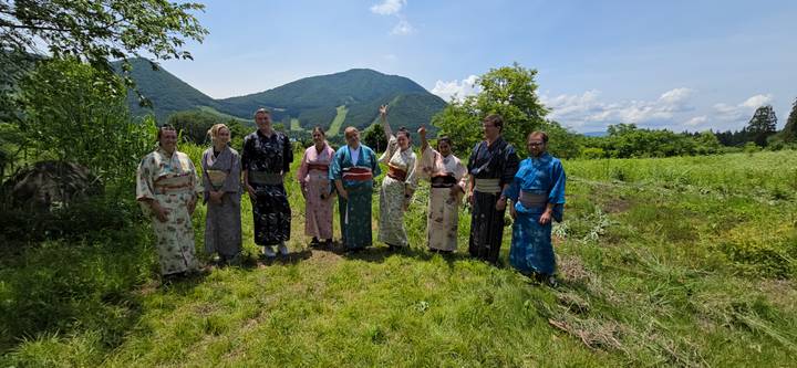 Group wearing colorful yukata pose in grassy field with rolling green mountains behind