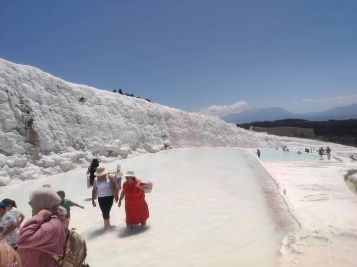 Visitors wading through turquoise pools along white travertine terraces