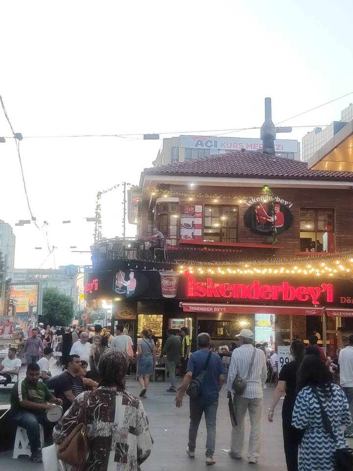 Busy street corner restaurant sign illuminated by string lights at dusk