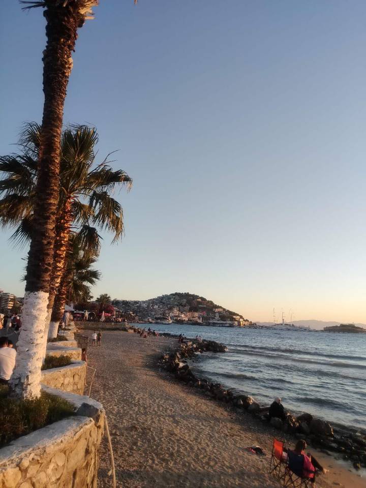 Palm-lined waterfront promenade at sunset with people relaxing by the sea