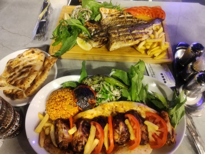 Plates of grilled fish, kebab, fries and fresh herbs on restaurant table