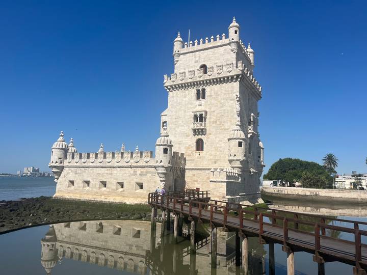 Iconic stone Belém Tower rising from the river edge with a wooden footbridge and vivid blue sky