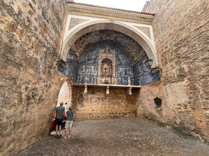 Stone archway decorated with blue azulejos and tourists admiring the artwork