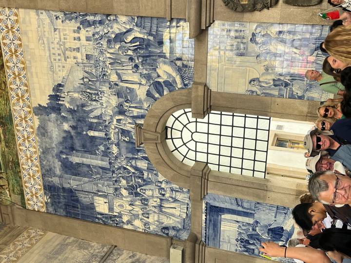 Crowded hall of São Bento Station displaying vast blue azulejo mural scenes