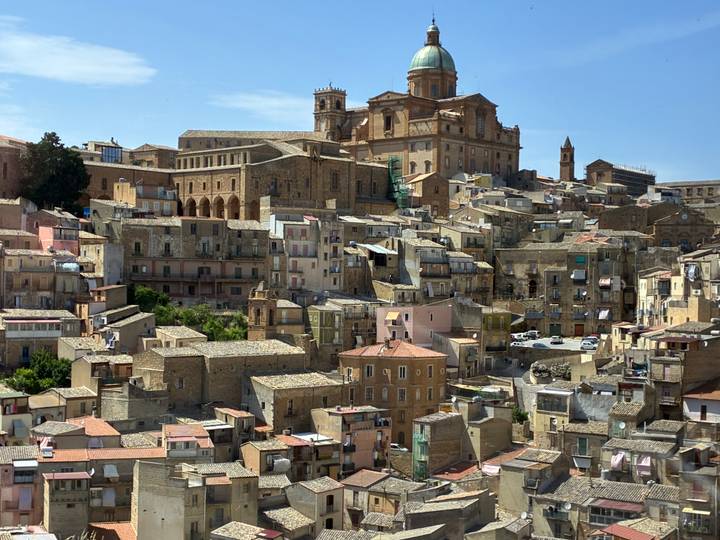 Panoramic view of a densely packed Sicilian hill town crowned by a large historic cathedral