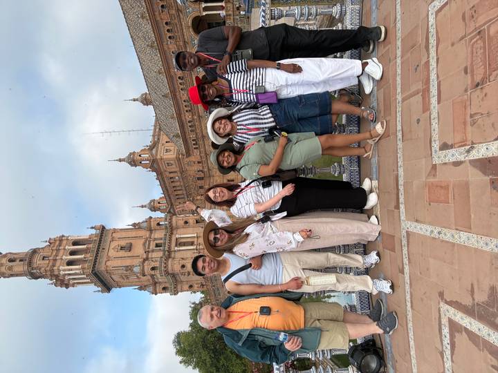 Larger tour group standing and smiling before the terracotta tower of Plaza de España in Seville.