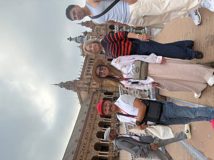 Three travellers posing beside the fountains of Plaza de España with the elaborate building behind.