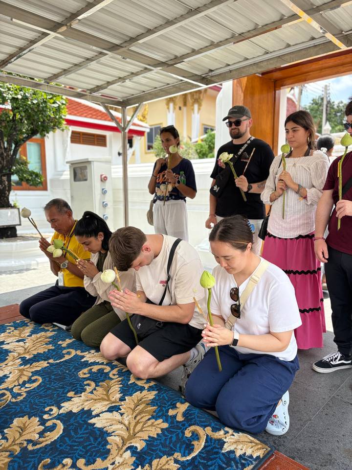 Travellers kneel with lotus buds during a traditional prayer ritual inside a Thai temple.