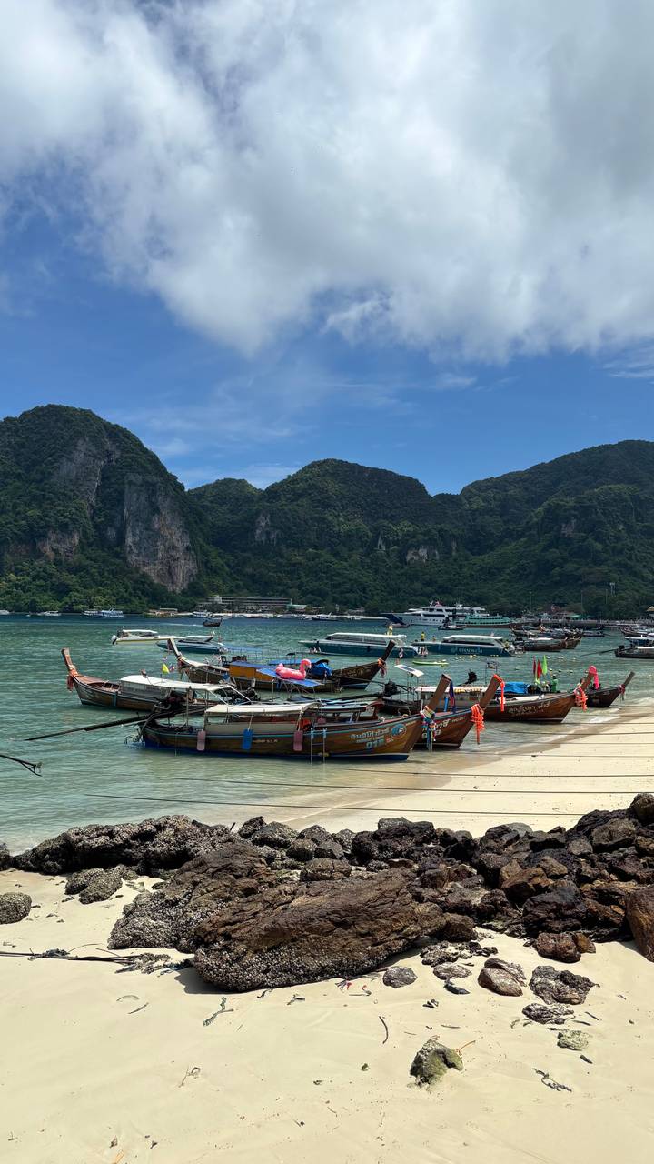 Traditional long-tail boats bob in a turquoise bay backed by dramatic limestone cliffs and jungle.