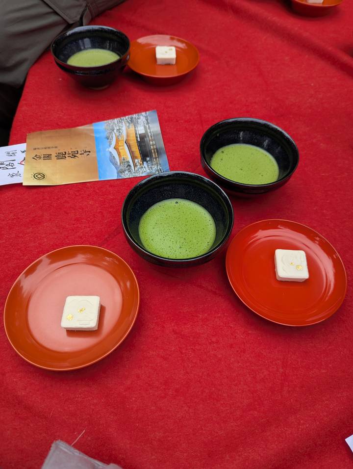 Three bowls of vibrant green matcha tea with small gold-leaf sweets on red lacquer trays.